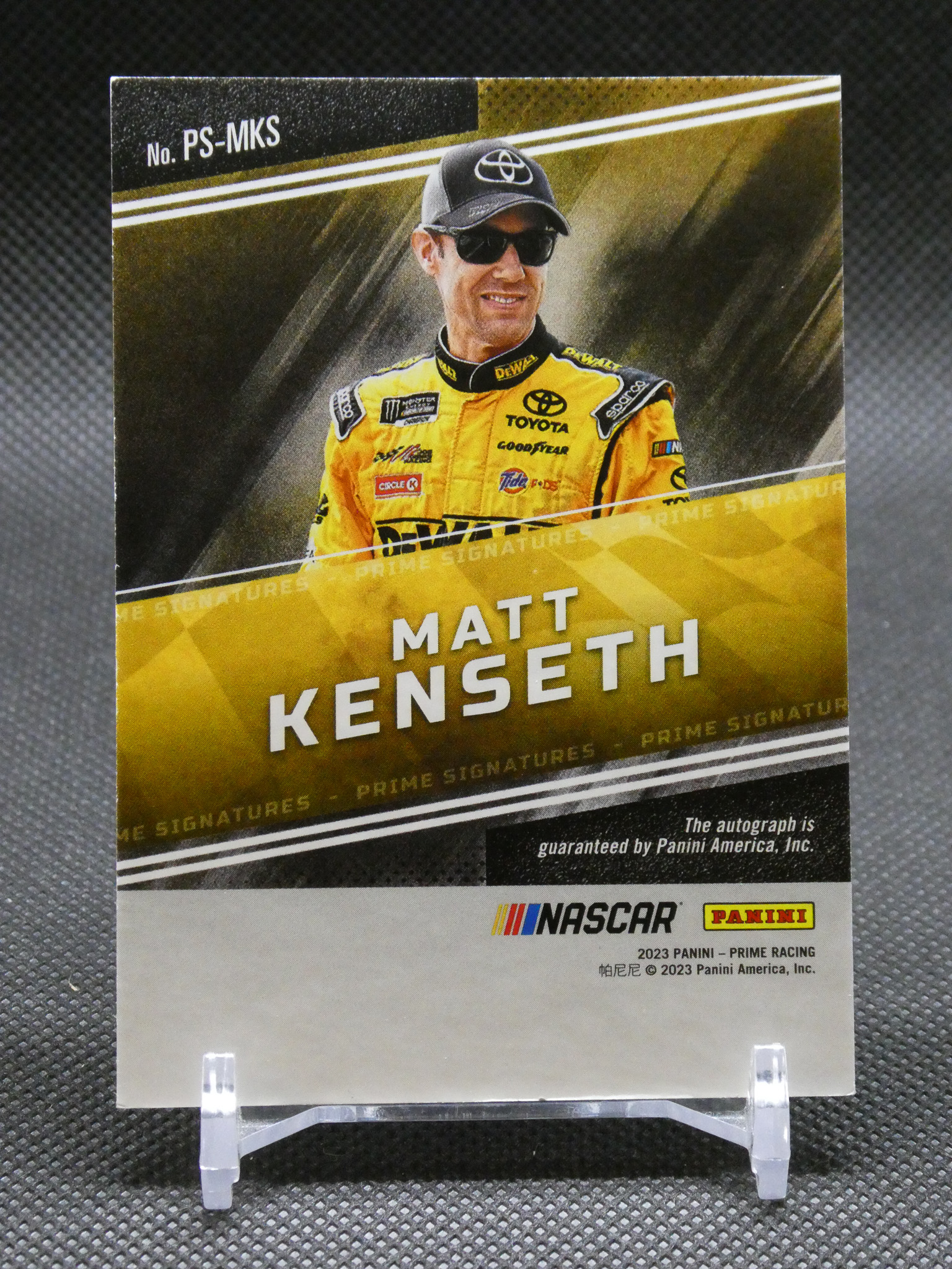 NASCAR Panini Prime Signatures card featuring Matt Kenseth in a yellow racing suit, smiling with sunglasses and cap, on display.