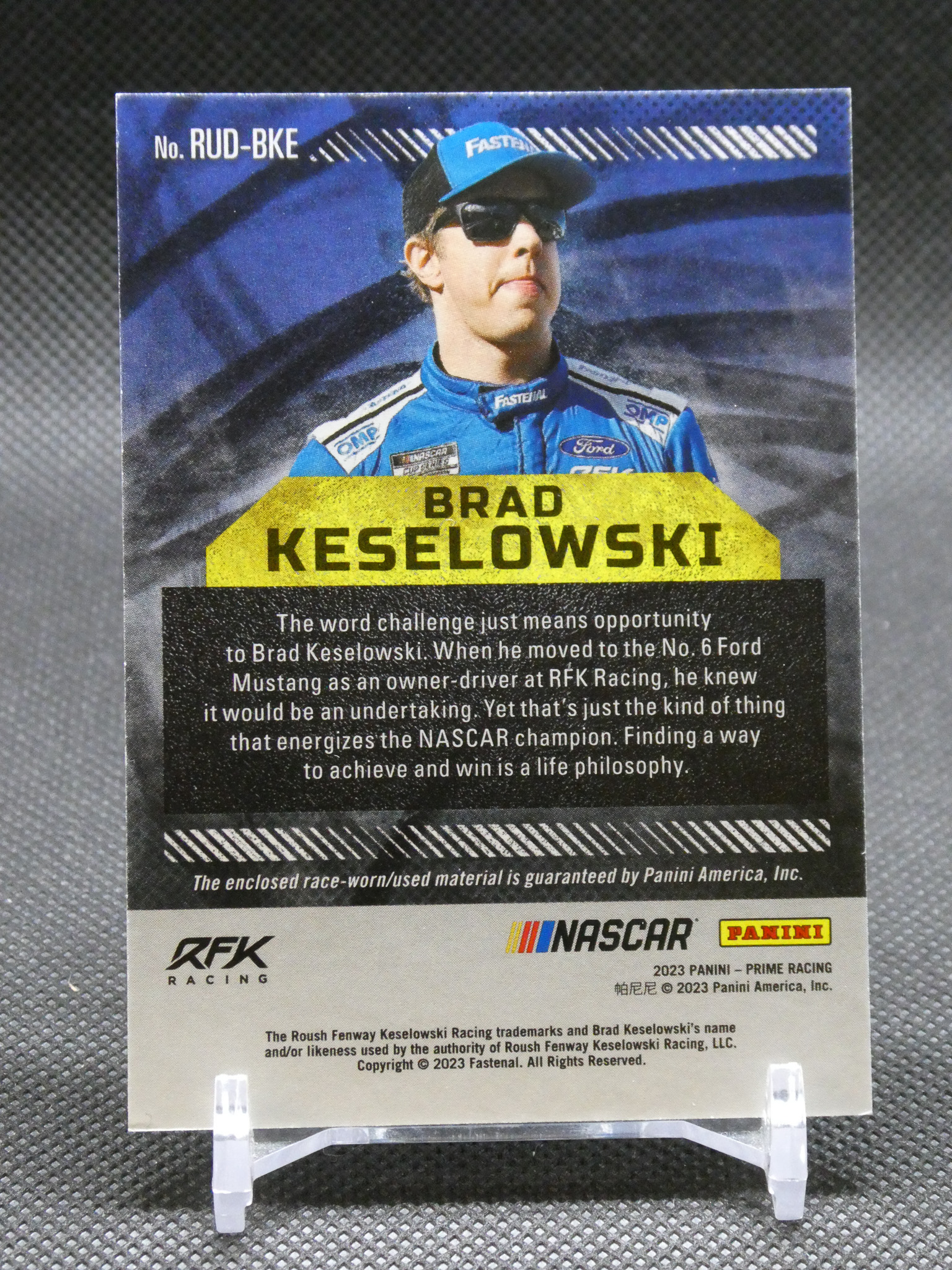 Back of a Panini NASCAR trading card featuring Brad Keselowski, with a blue racing suit, yellow name label, and a biographical paragraph.