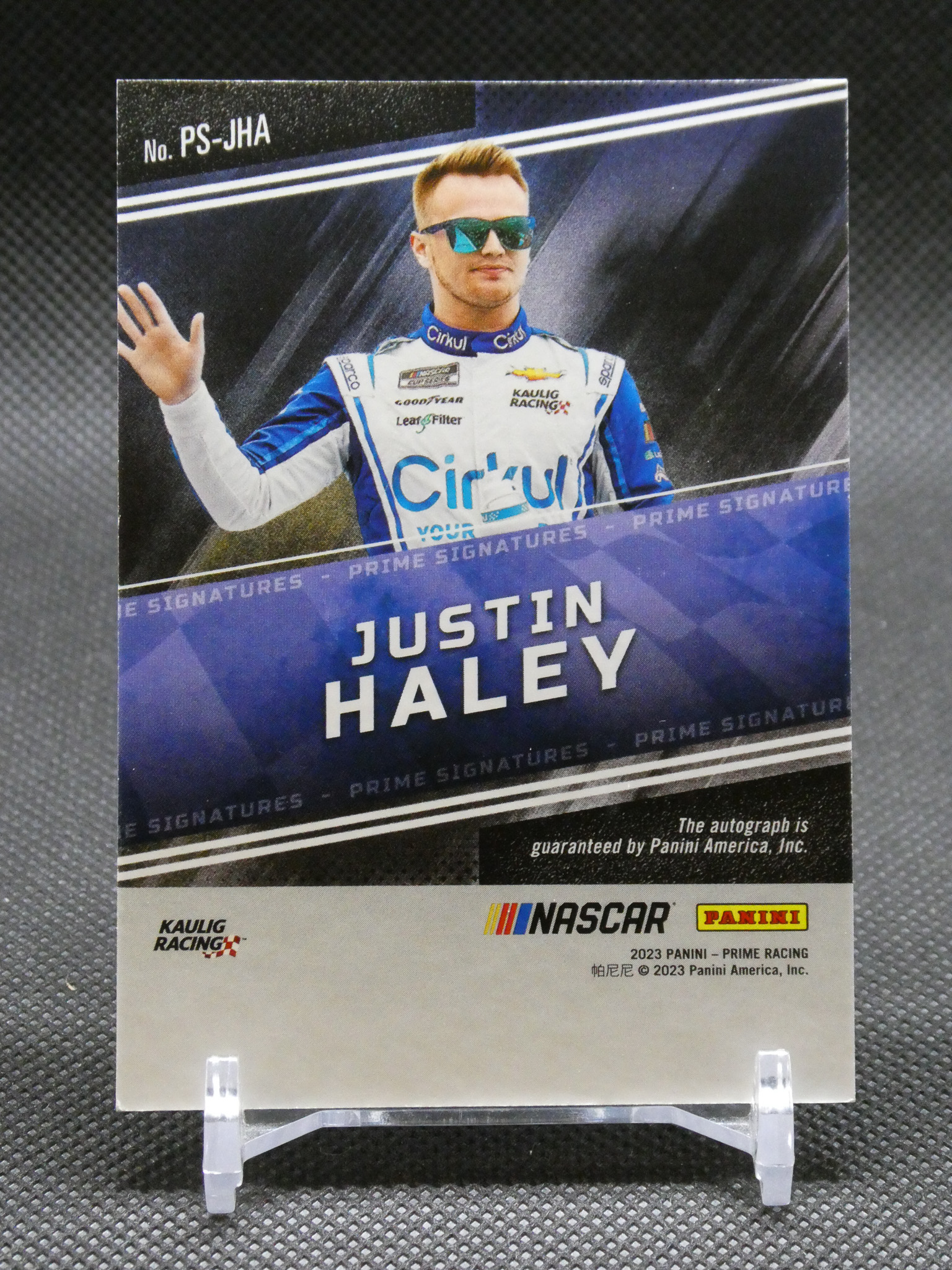 Autographed NASCAR Panini card of Justin Haley, in blue-and-white racing suit, waving at the camera with his name prominently displayed.