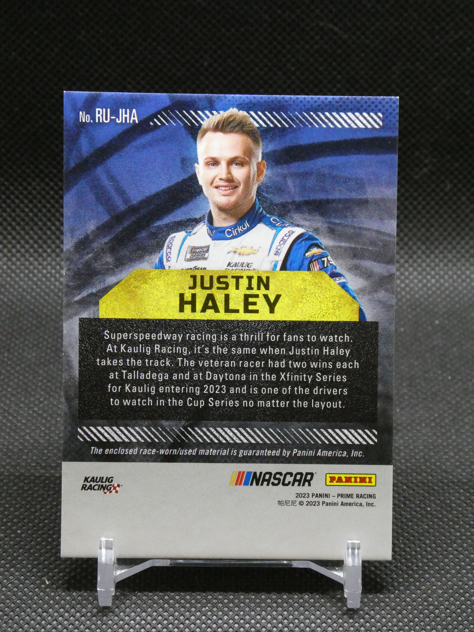 Trading card image of NASCAR driver Justin Haley in a blue racing suit, with his name on a yellow label.