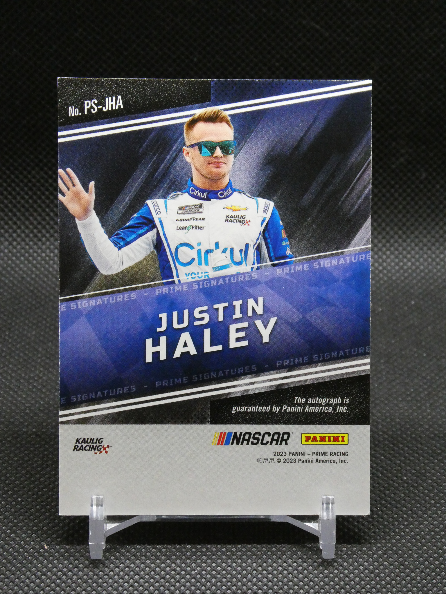Panini NASCAR autograph card featuring Justin Haley in a blue racing suit, waving from a presentation pose