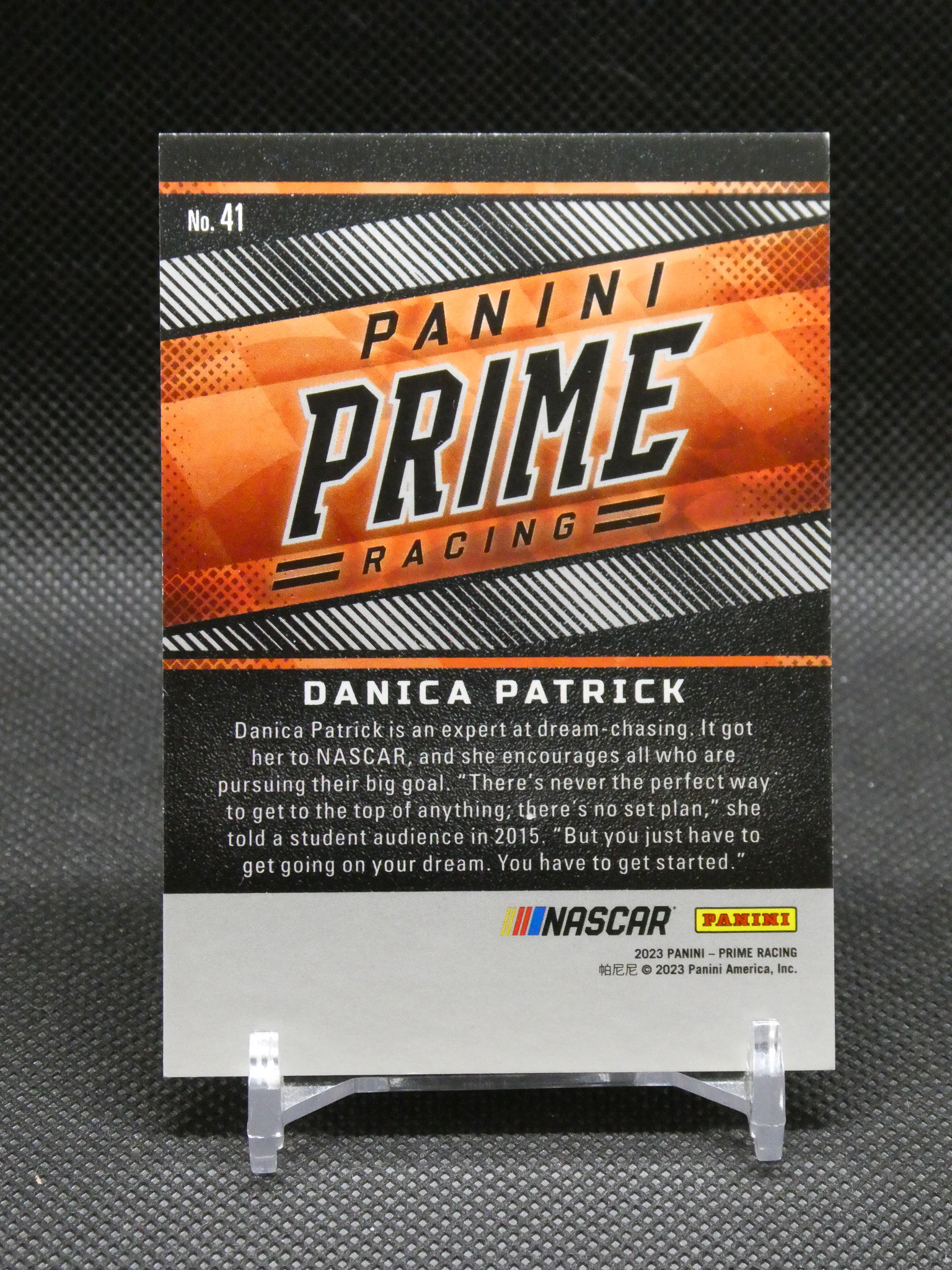 Back of a Panini Prime Racing trading card for Danica Patrick, with orange and black diagonal graphics and a bio paragraph visible.