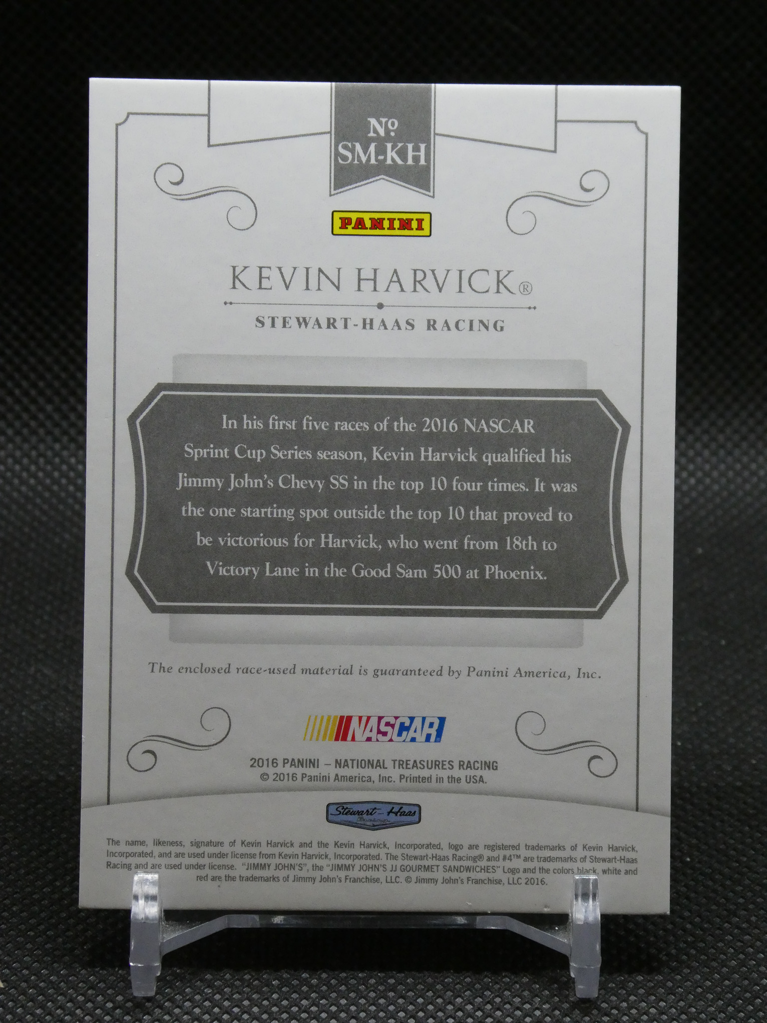 Black-and-white Panini collectible card featuring Kevin Harvick and the Stewart-Haas Racing logo, displayed on a stand.