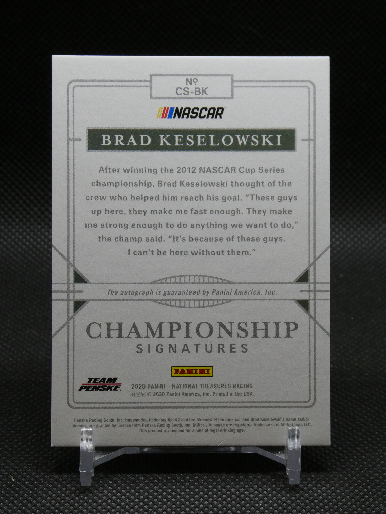 Panini NASCAR Championship Signatures card featuring Brad Keselowski, with NASCAR logo and a quote, on a display stand.