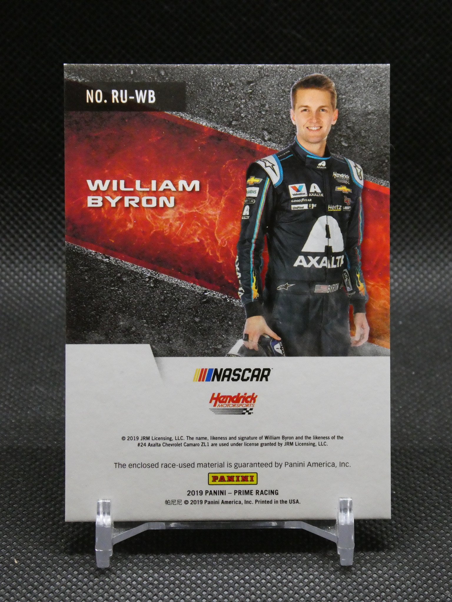 Trading card featuring NASCAR driver William Byron in a black Axalta racing suit, standing against a fiery red and black background with sponsor logos and his name prominently displayed on the card surface.",