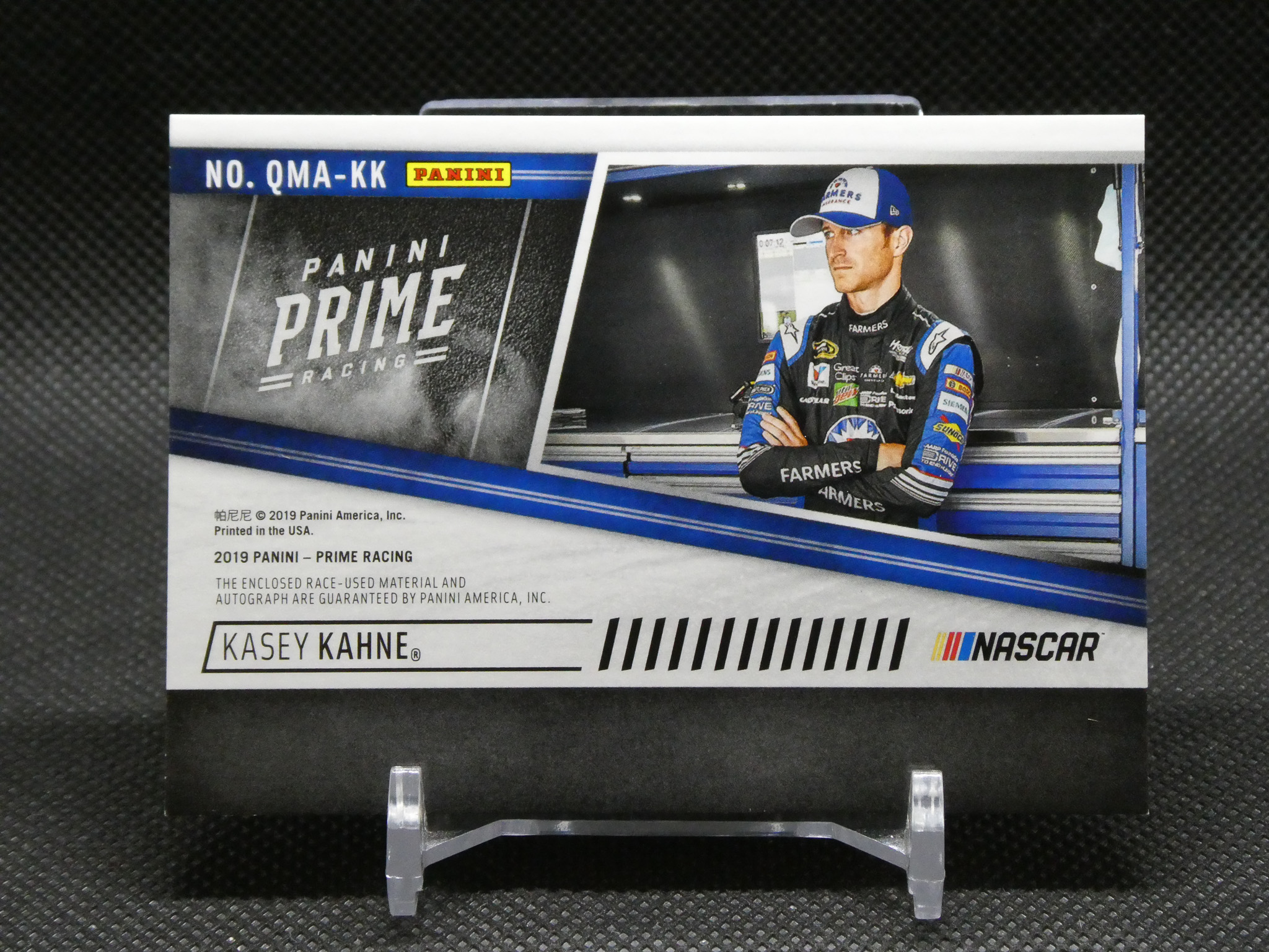 Panini Prime Racing collectible card showing NASCAR driver Kasey Kahne in a racing suit with blue branding, posed with arms crossed.