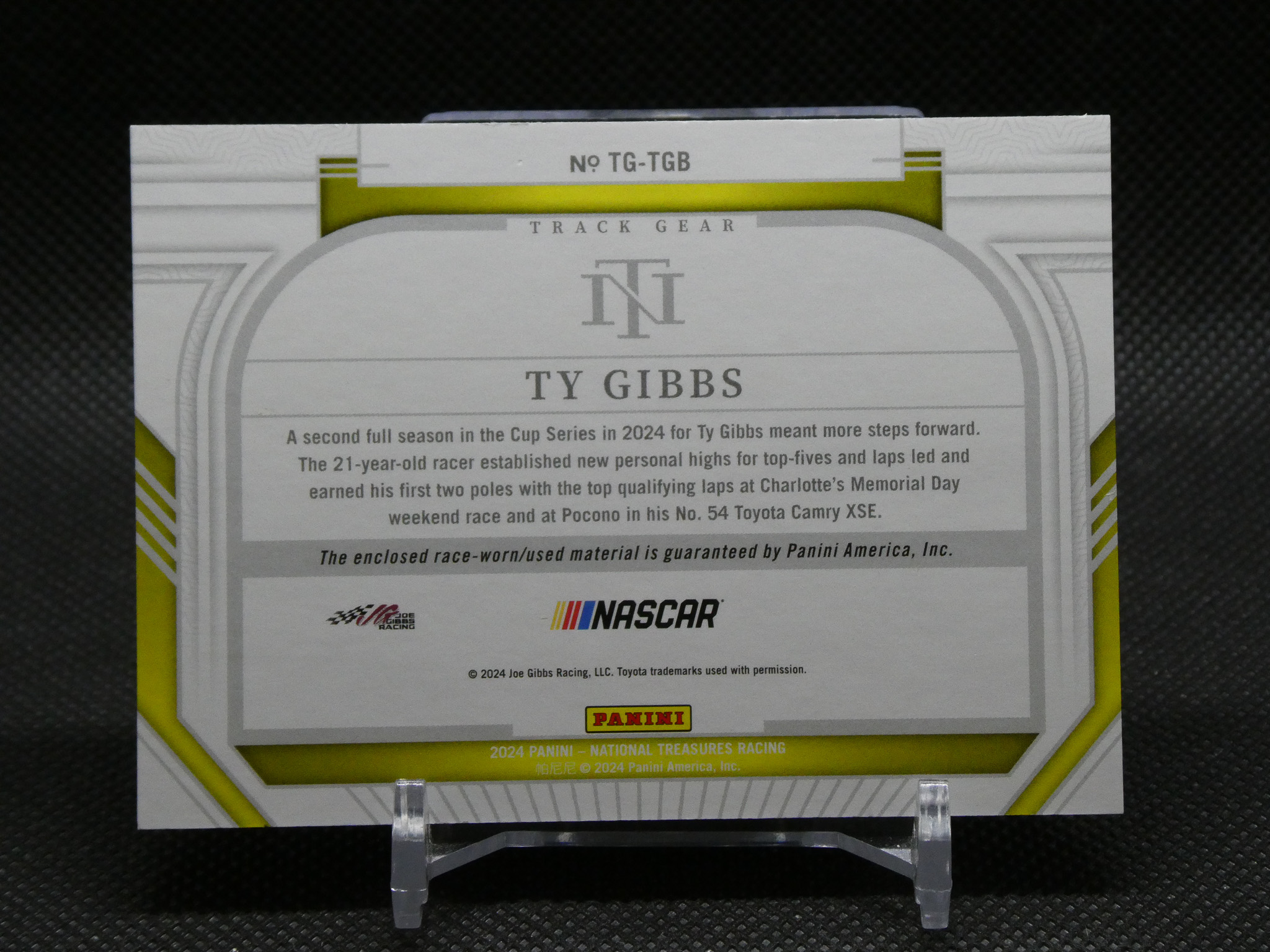 Back of a Ty Gibbs NASCAR trading card on a display stand, with gray decorative frame, Panini and NASCAR logos visible.