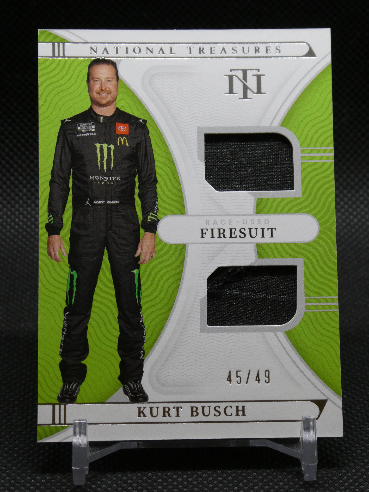 Trading card featuring Kurt Busch in a black Monster Energy firesuit with sponsor logos, lime-green design, two fabric swatches, 45/49.