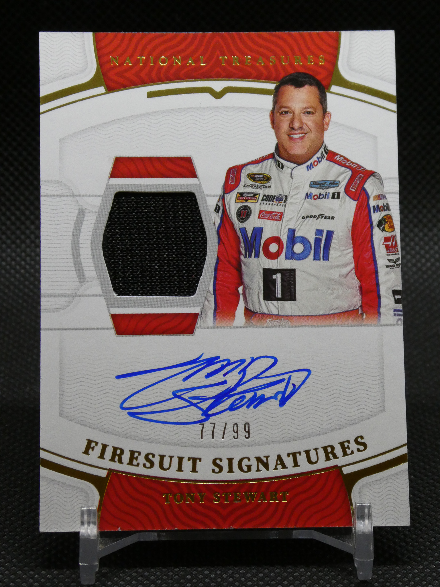 Front of a NASCAR card showing Tony Stewart in a Mobil 1 racing suit with a red-and-white design and a cutout helmet insert; signatures visible below.