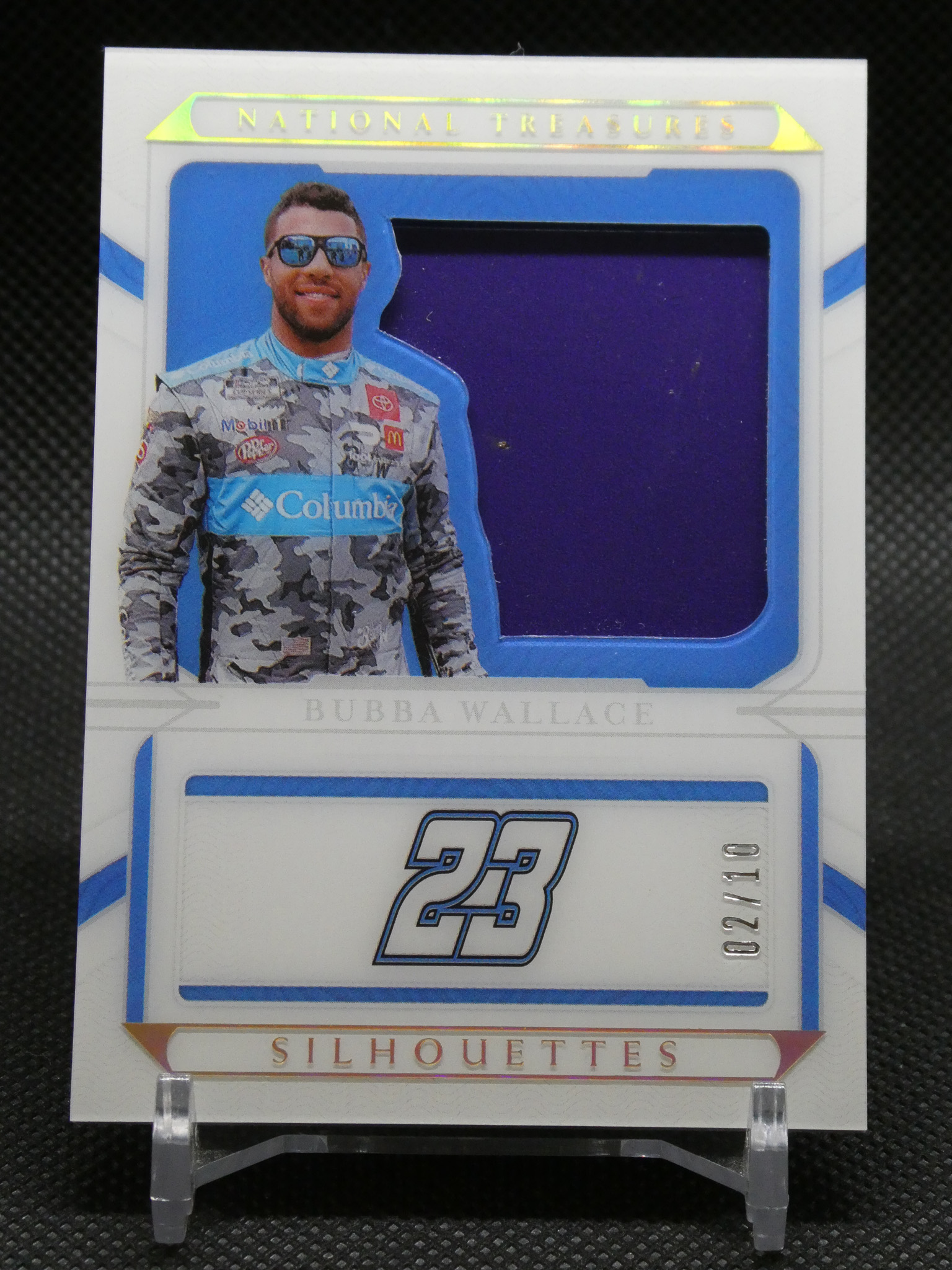 Front of a sports trading card package showing a life-size cutout of a race driver in a camo suit with sunglasses, blue and white design, and 'NATIONAL TREASURES' at the top along with a blue window and the word 'SILHOUETTES' at the bottom.