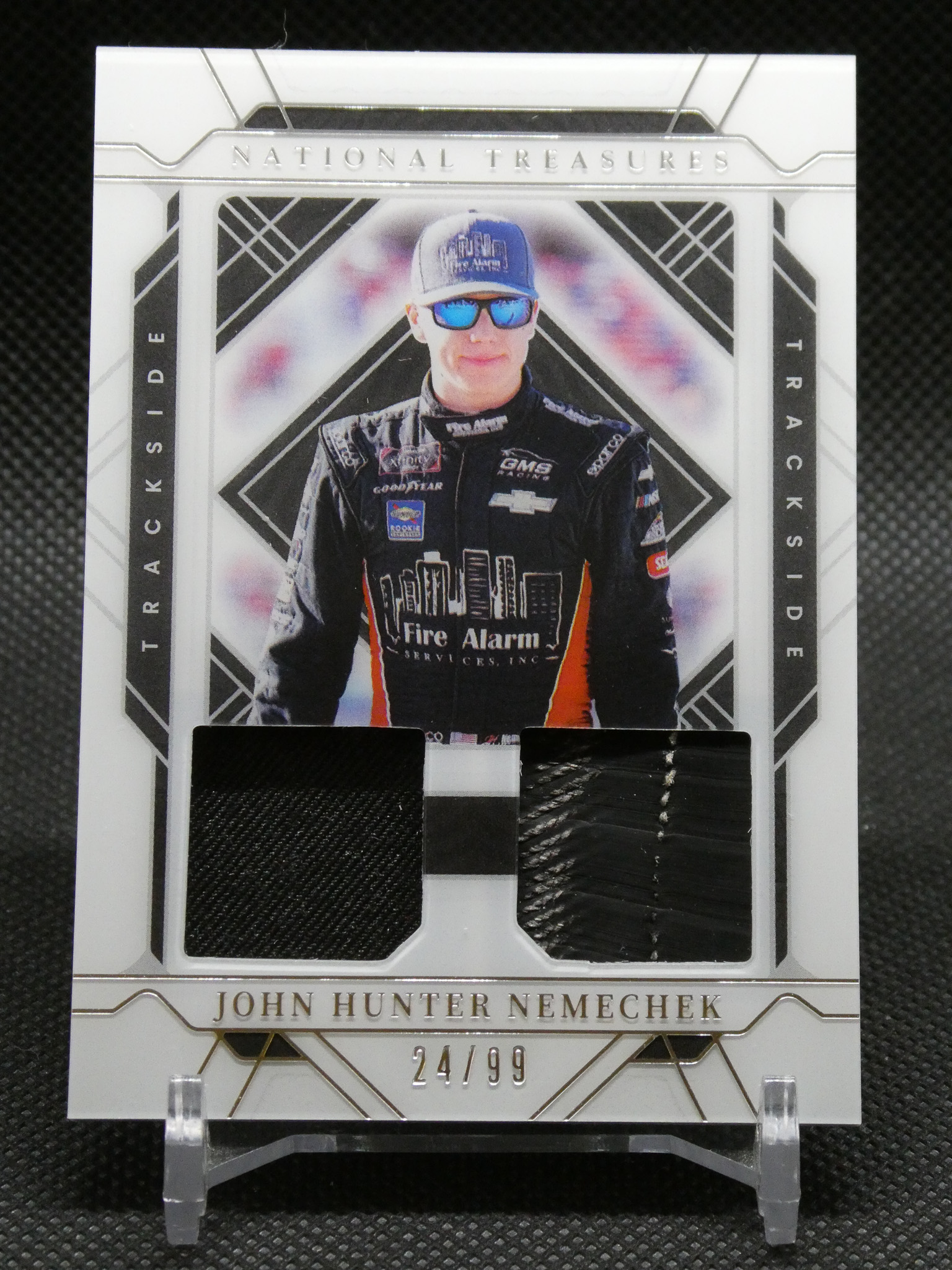 Trading card featuring race car driver John Hunter Nemechek in a black racing suit and blue sunglasses, with 'National Treasures' branding and edition 24/99