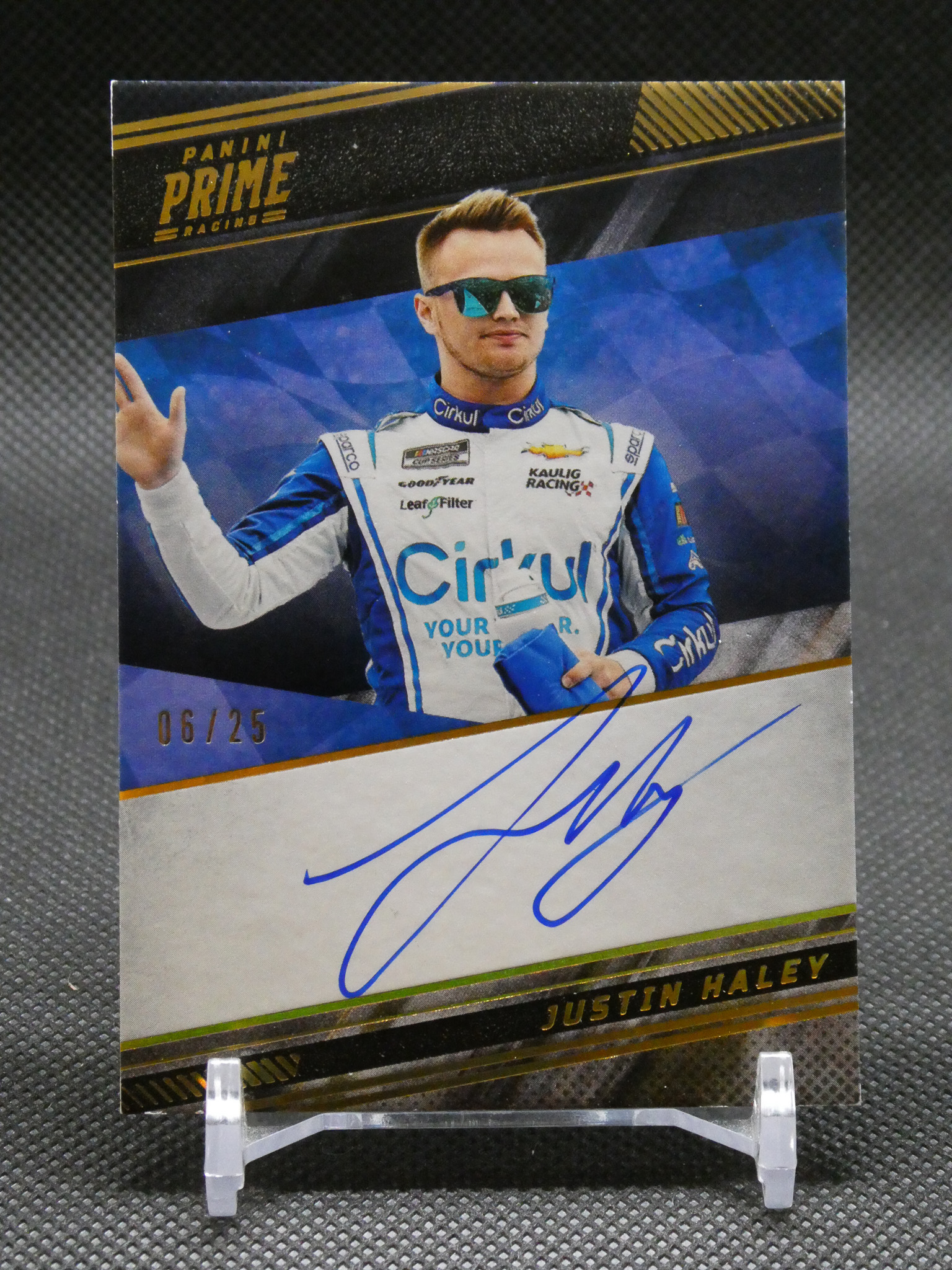 Autographed Panini Prime Racing card showing a driver in blue-and-white suit with sunglasses; signature across bottom edge.