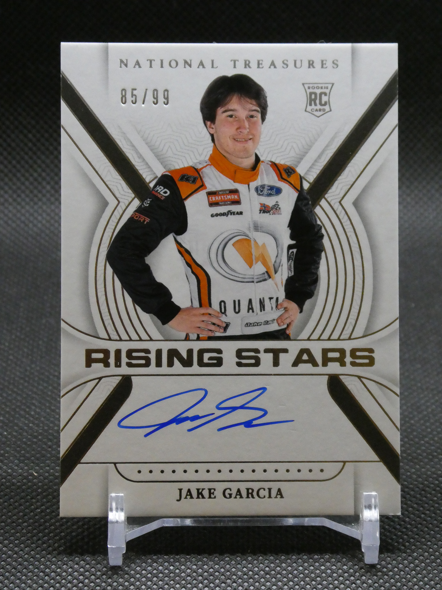 Autographed trading card of Jake Garcia in a white-orange racing suit, labeled 'Rising Stars' with National Treasures branding and a blue autograph.