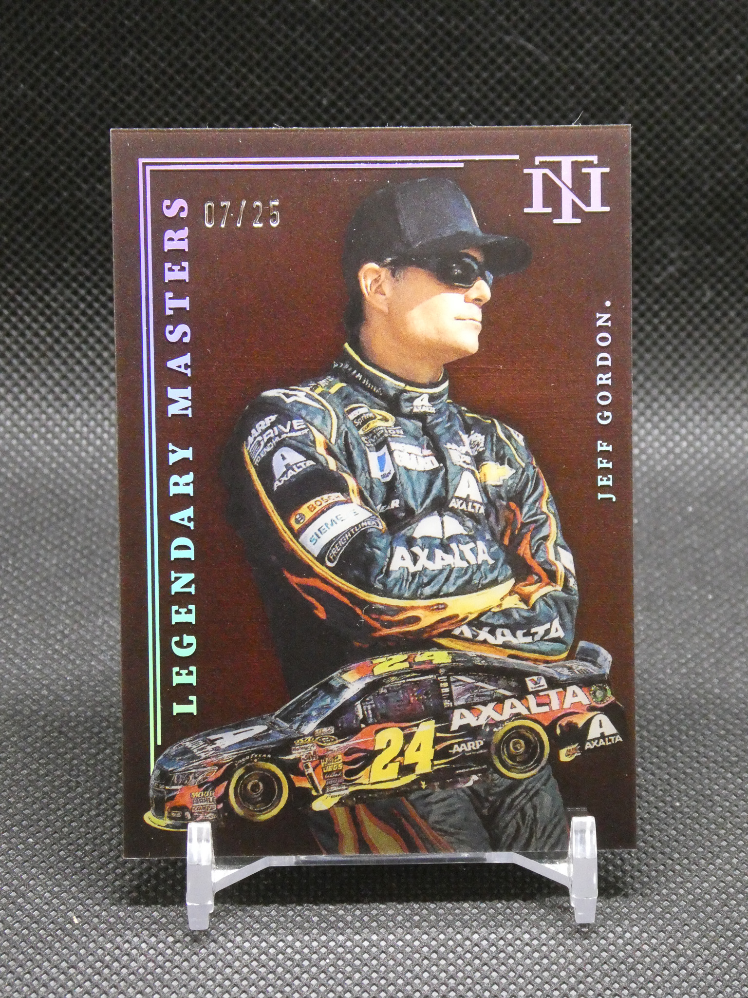 NASCAR trading card portrait of a driver in a black cap and sunglasses, with a #24 race car graphic at the bottom on a display stand.