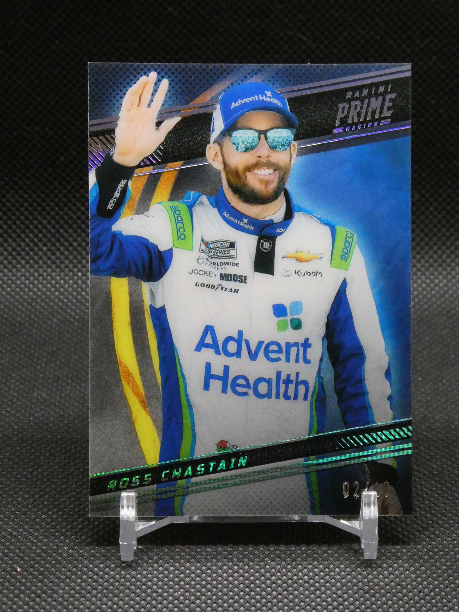 Poster of NASCAR driver Ross Chastain waving, wearing a blue Advent Health racing suit and cap with mirrored sunglasses, mounted on a display stand.