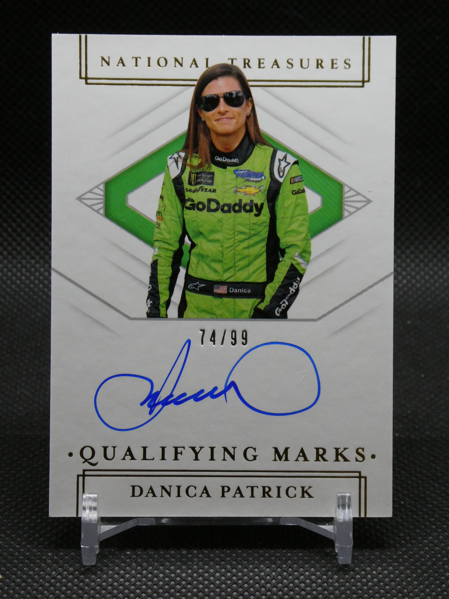 Autographed trading card image of Danica Patrick in a green GoDaddy racing suit, showing 74/99 and National Treasures branding in the background