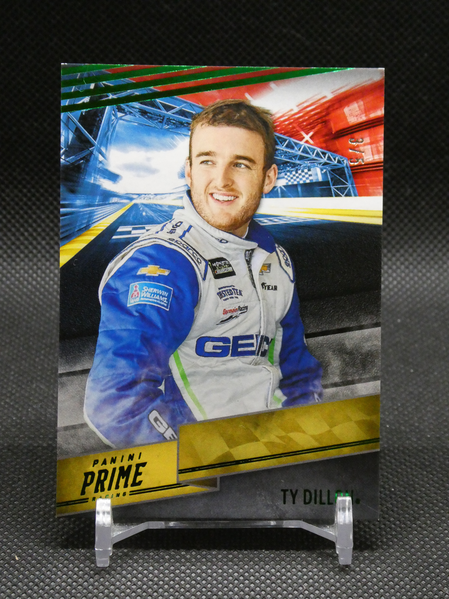 Portrait of a smiling race car driver in a blue and white suit on a glossy poster with Panini Prime branding in the foreground.