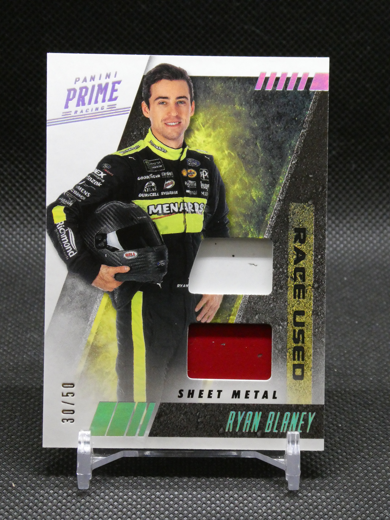 Trading card featuring NASCAR driver Ryan Blaney in a black neon-yellow racing suit with Panini Prime Racing branding and a red insert window.
