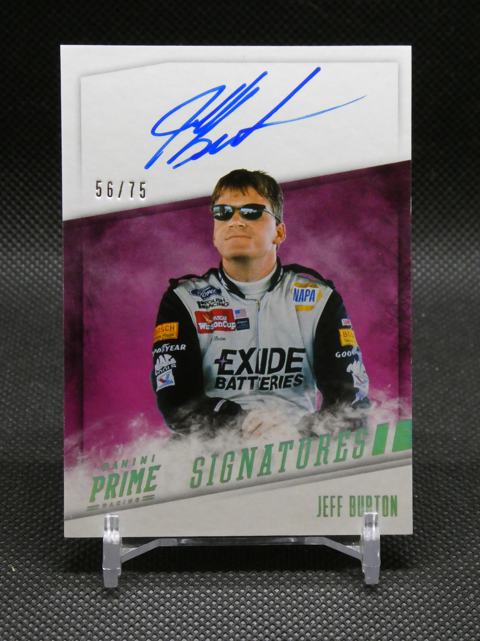 Autographed racing poster: blue signature on white card above a driver in a white racing suit with sunglasses, purple backdrop, 56/75 edition badge visible.