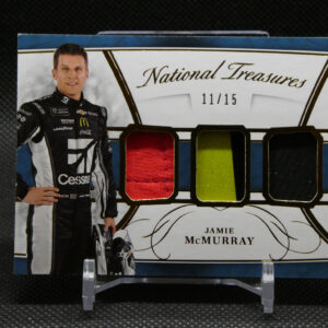 Portrait of NASCAR driver Jamie McMurray in a racing suit standing beside a display labeled 'National Treasures' with color swatches (red, yellow, green).
