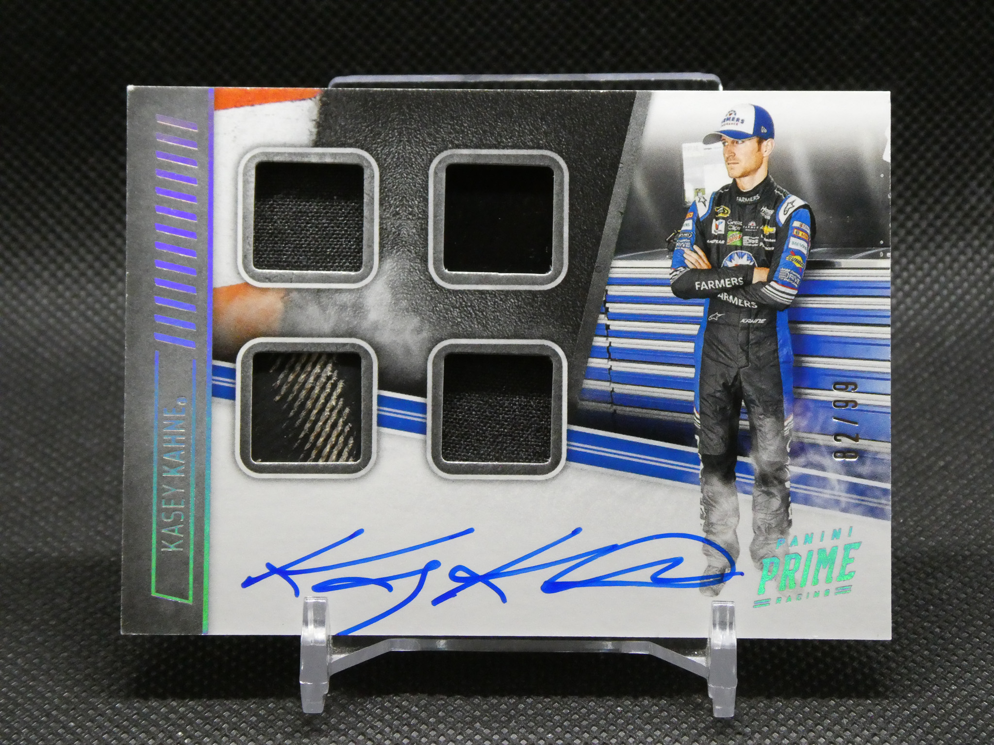 Autographed racing card showing a driver in a blue-and-black suit beside a garage backdrop, blue signature across the bottom