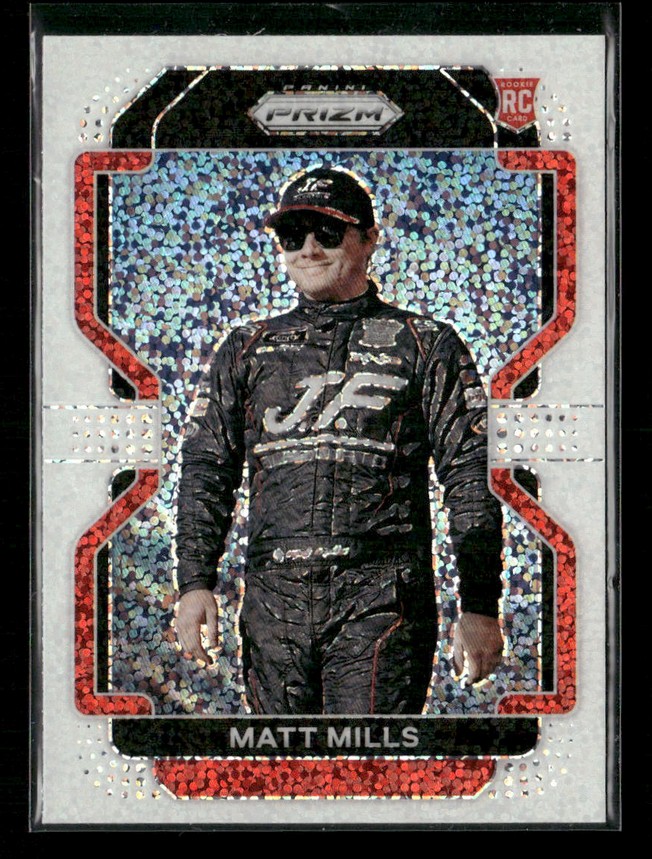 Holographic trading card featuring race car driver Matt Mills in a black racing suit and cap, standing with hands at his sides; 'MATT MILLS' shown at the bottom, with a rookies/RC marking near the top right.