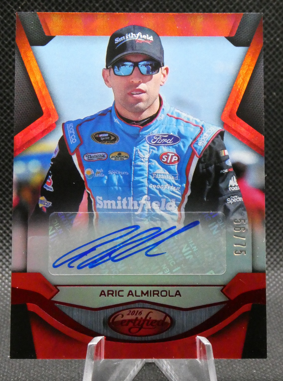 Autographed 2016 Certified NASCAR trading card of Aric Almirola in a blue Smithfield race suit with cap and sunglasses; blue signature panel.