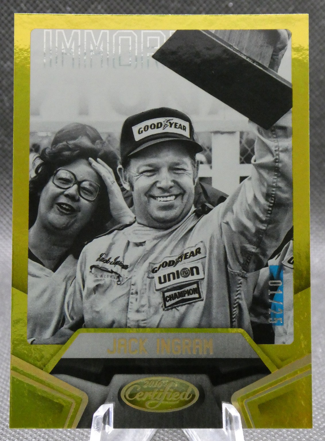 Smiling race car driver in a Goodyear cap and uniform, raising his arm, with a woman beside him.