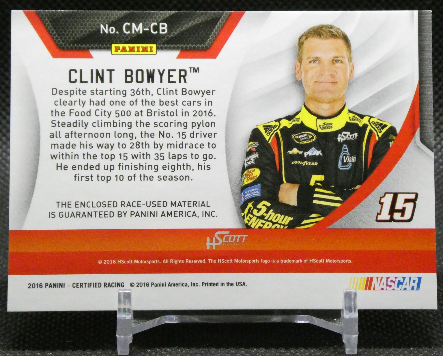 Panini NASCAR trading card featuring Clint Bowyer, with a bio paragraph on the left and Bowyer in a yellow-black racing suit on the right, number 15 visible.