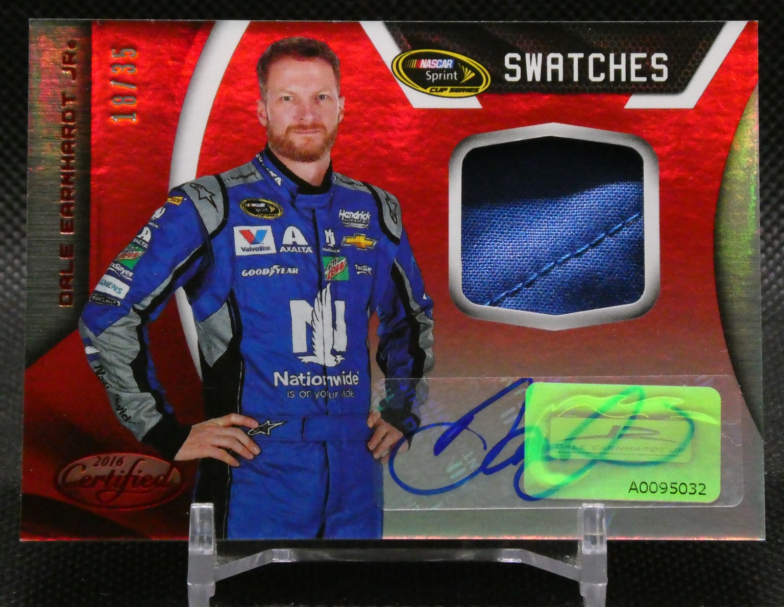 Trading card featuring a NASCAR driver in a blue suit with a blue fabric swatch and autograph on a red background.