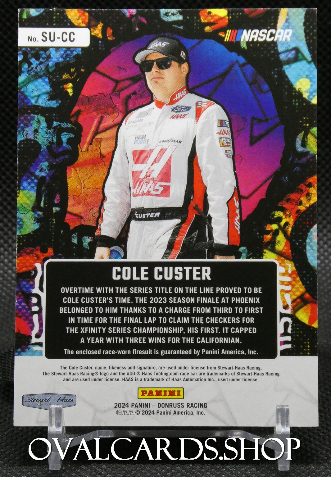 Trading card of Cole Custer, NASCAR driver, in a white Haas racing suit with a vibrant graffiti backdrop.