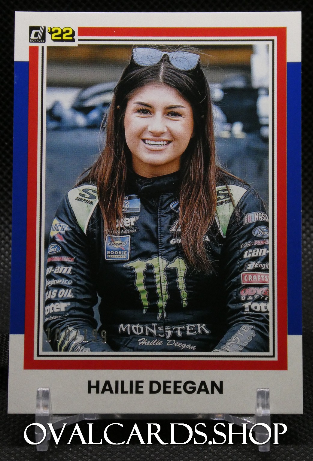 Trading card portrait of racer Hailie Deegan in a Monster Energy racing suit with sponsor patches, smiling at the camera.