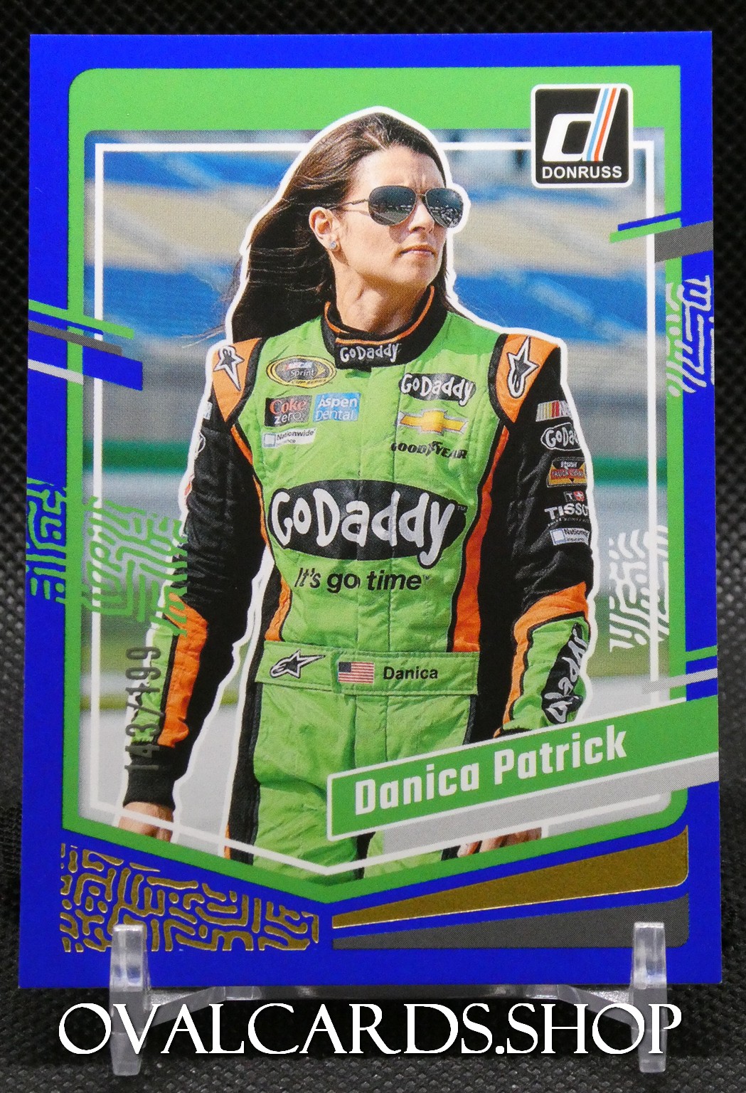 Trading card showing a female race car driver in a neon-green GoDaddy racing suit with sponsor logos and a bold blue border.
