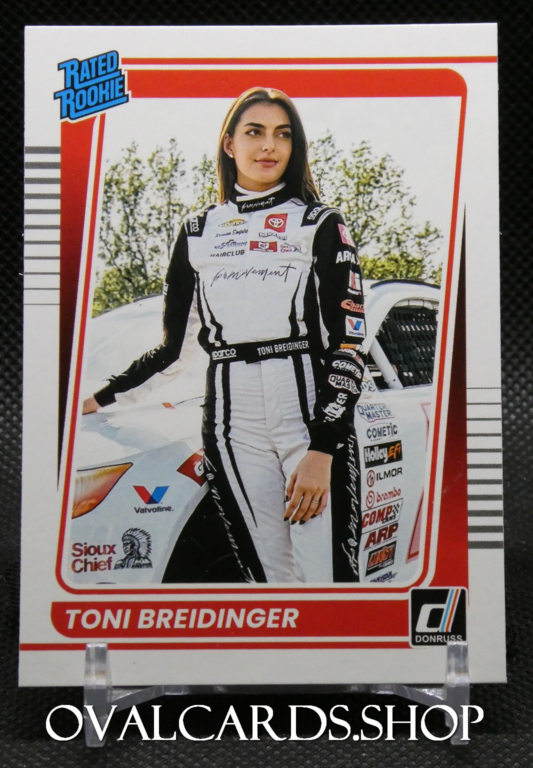 Racing trading card of Toni Breidinger, standing in a black-and-white racing suit with a race car behind her.