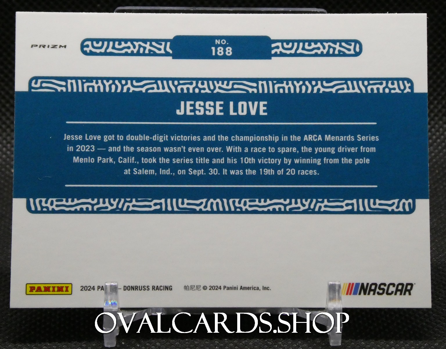Back of a Panini NASCAR trading card for Jesse Love, showing a blue banner with 'JESSE LOVE' and a descriptive bio text area with white decorative borders on top and bottom.