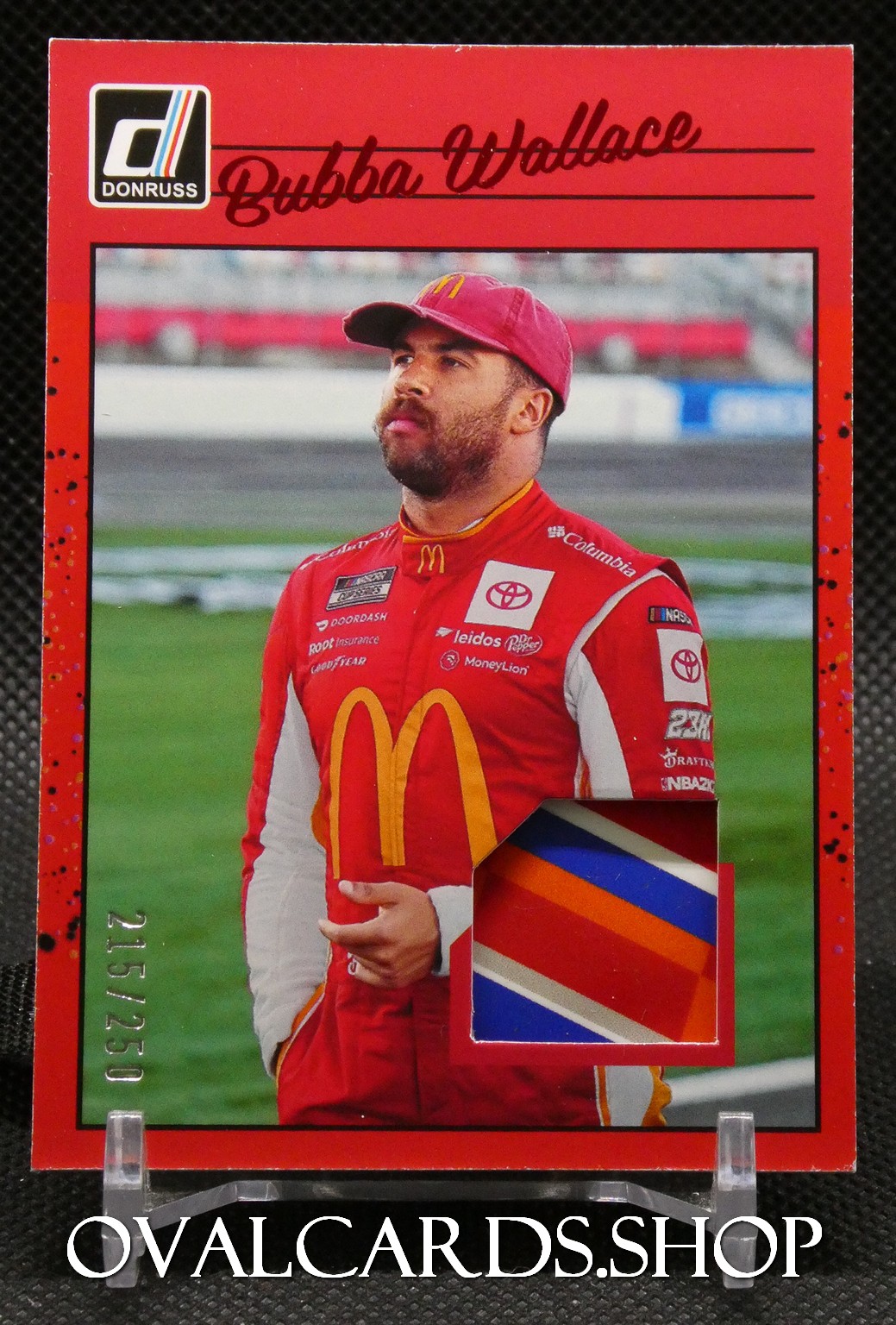 Trading card featuring NASCAR driver Bubba Wallace in a red McDonald's racing suit, with a color swatch patch on the lower right and a race track background.