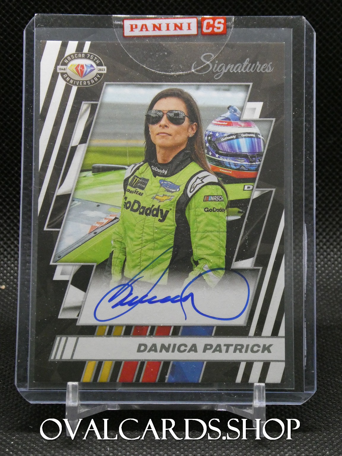 Trading card: Danica Patrick in a lime-green GoDaddy racing suit with autograph on the card and a racing helmet in the background (Panini Signatures).
