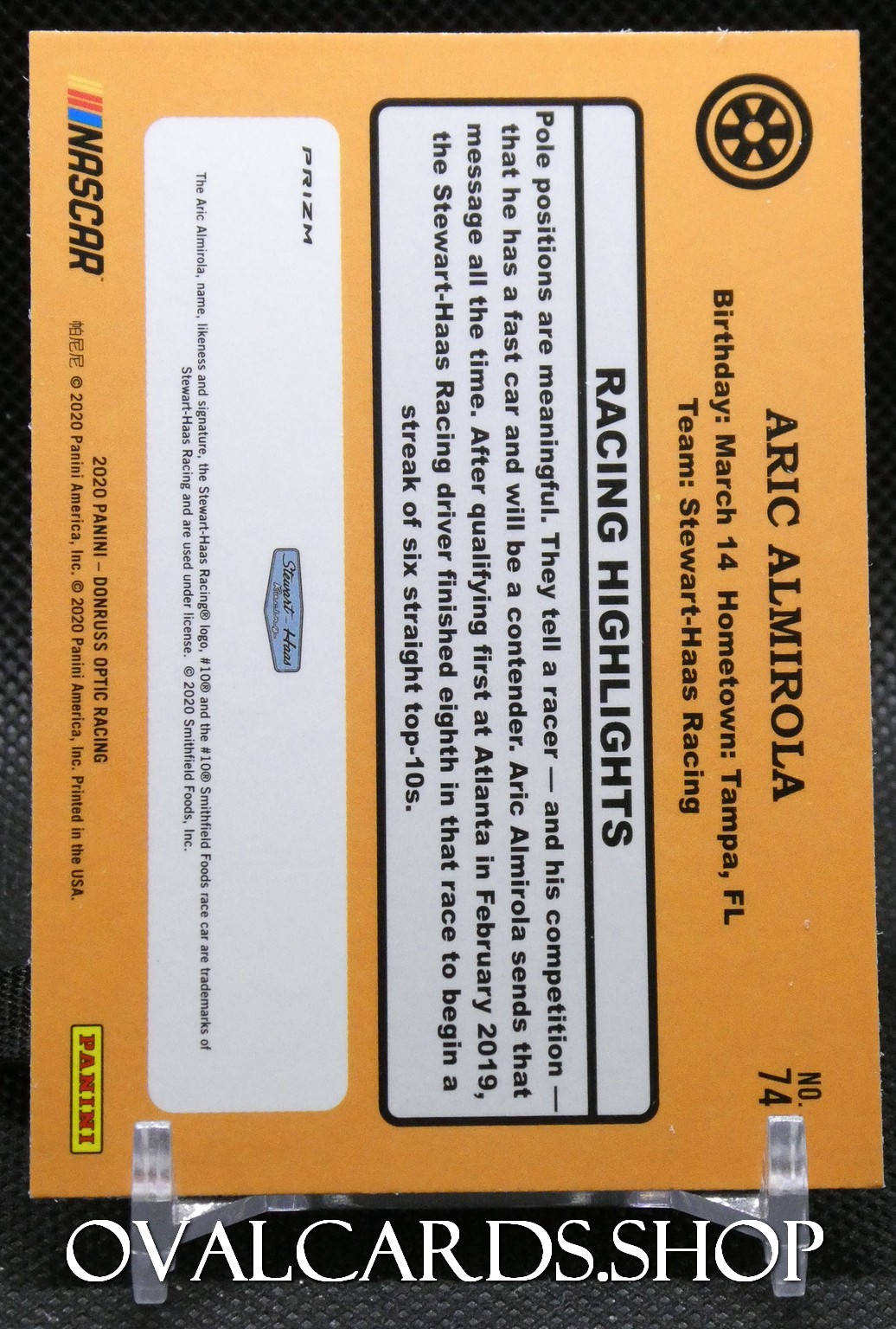 Orange NASCAR trading card featuring a 'RACING HIGHLIGHTS' panel and wheel icon, with text about ARIC AMIROLA and a hero image area on the left.