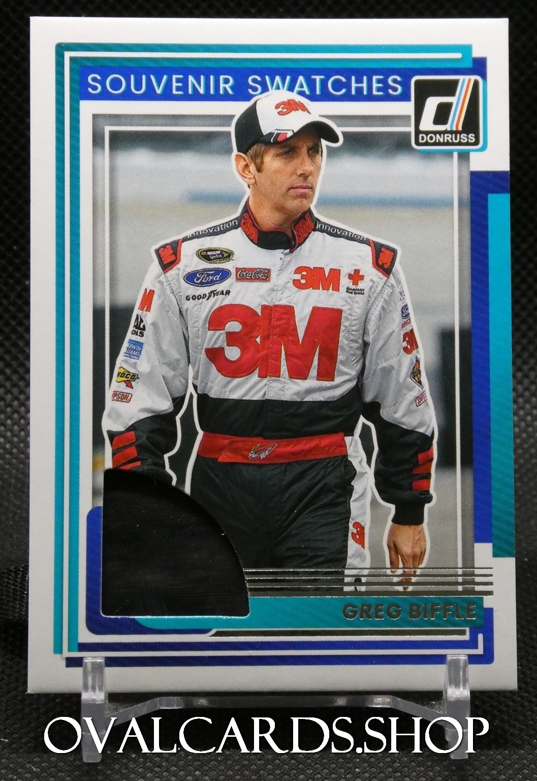 Trading card of race car driver Greg Biffle in a 3M racing suit, blue and teal border, 'Souvenir Swatches' at top, Donruss logo right, partial cutout window bottom left.