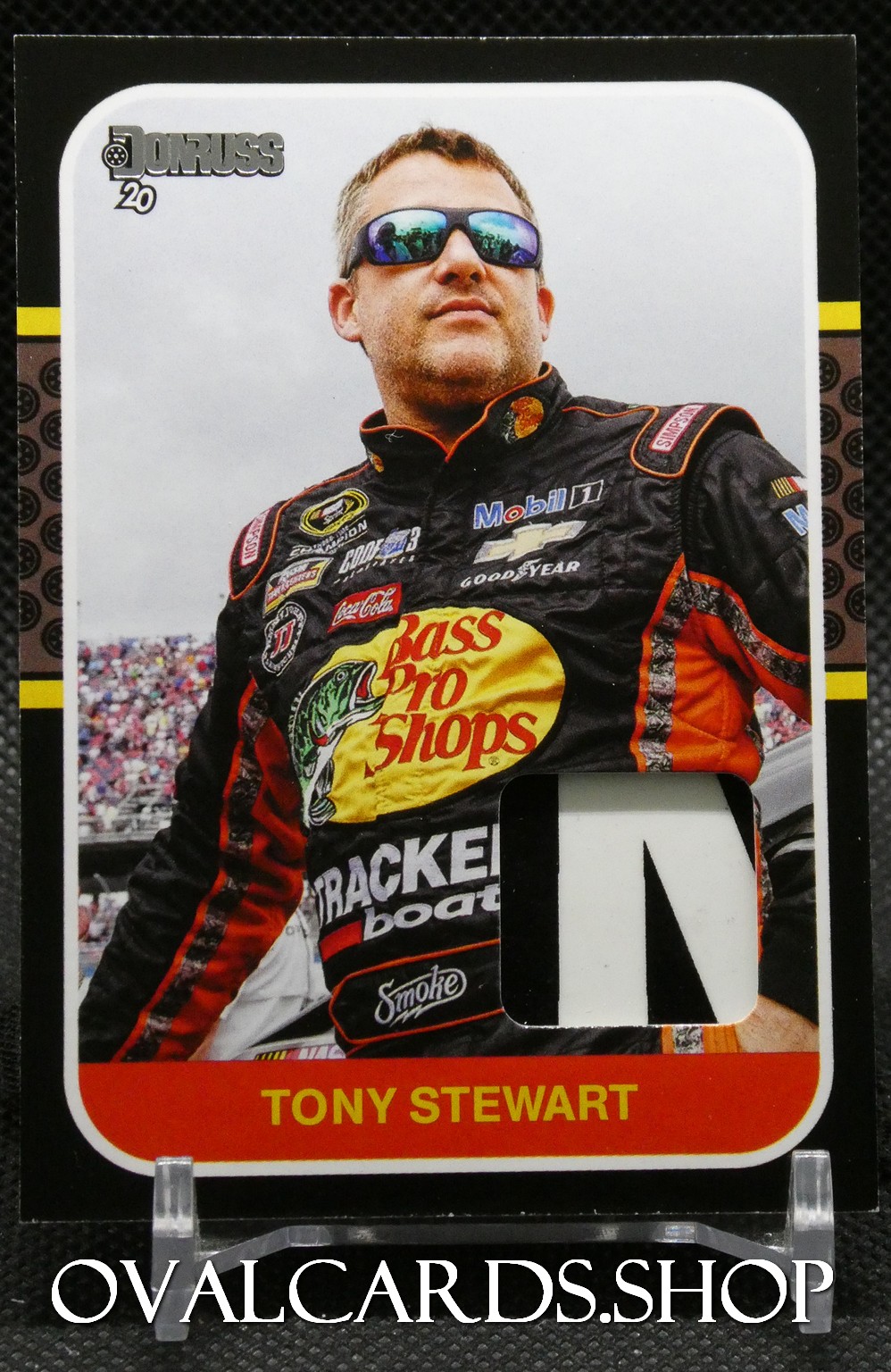 Trade card showing Tony Stewart in a black and orange Bass Pro Shops racing suit, wearing sunglasses, with sponsor logos visible on the suit.