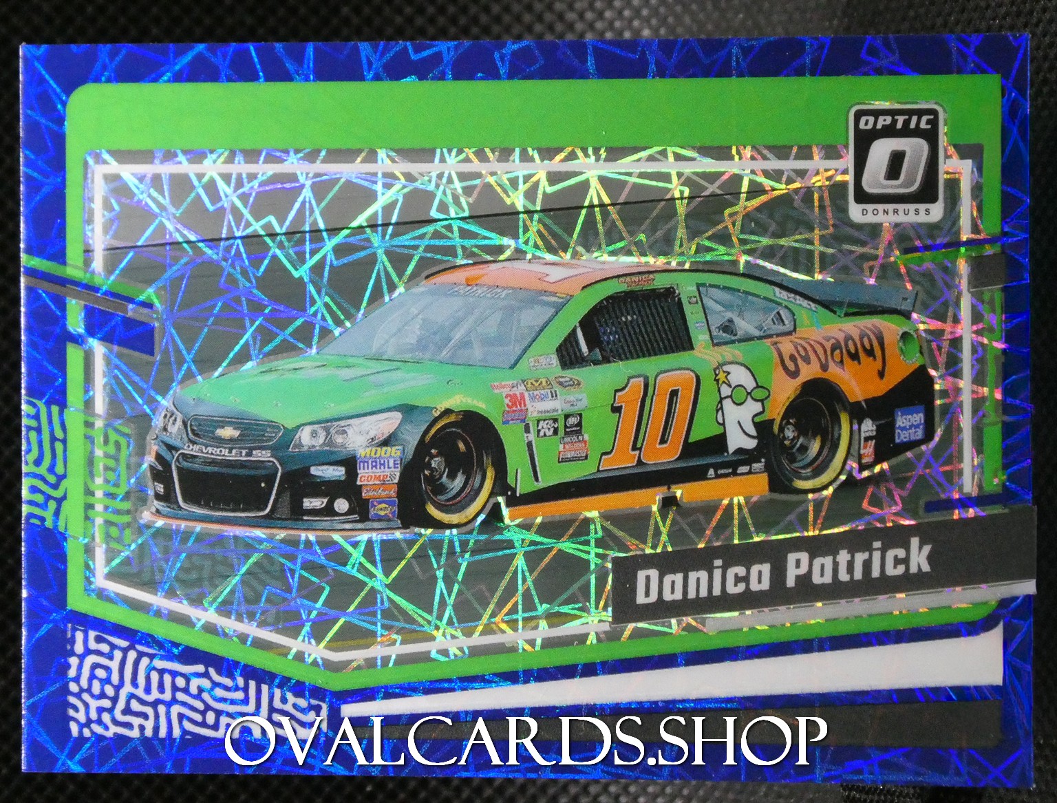Die-cast race car packaging showing a green/orange No. 10 car (Danica Patrick) with a holographic background and OvalCards.shop watermark.