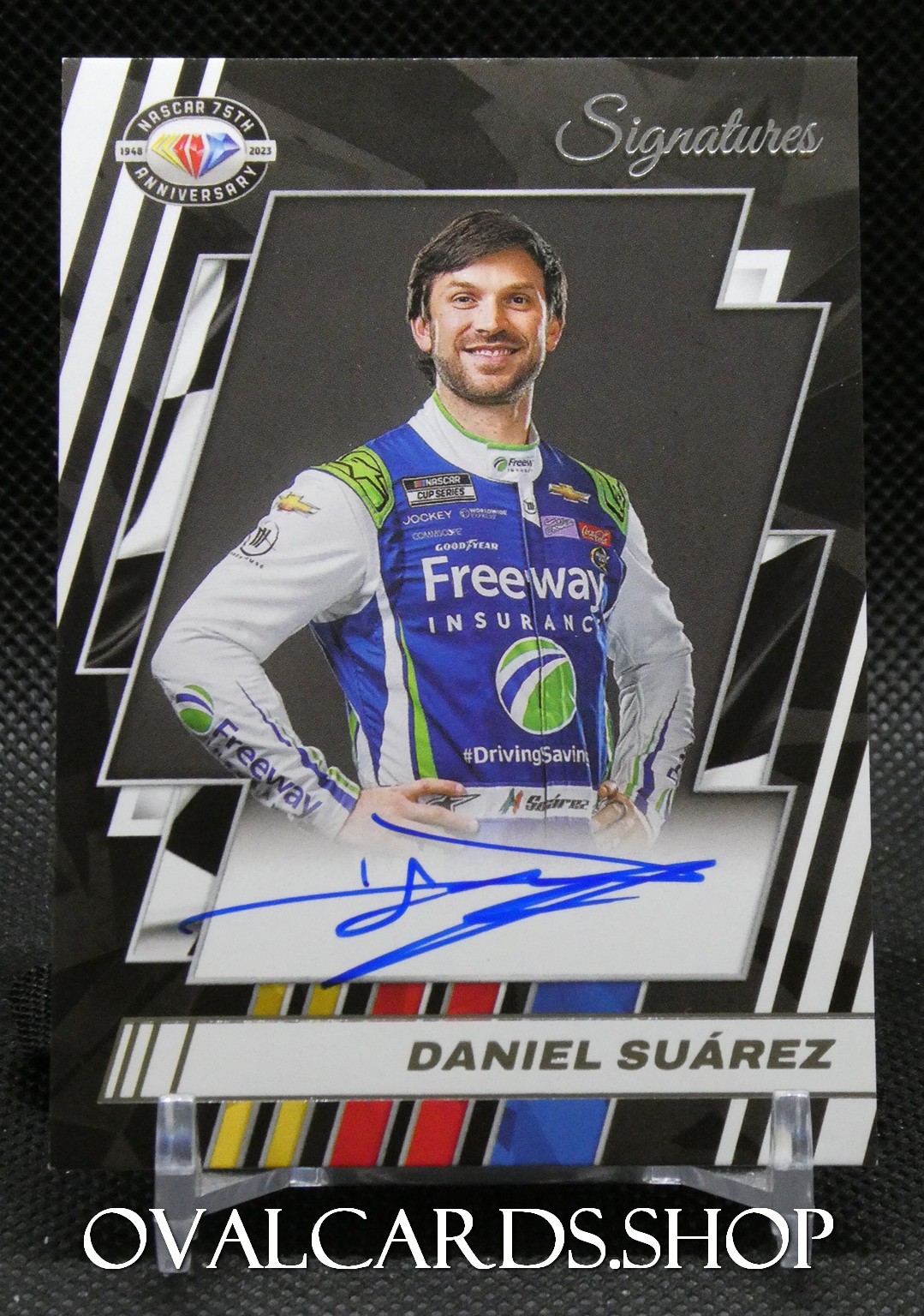 Autographed Daniel Suárez trading card showing him in a blue and white NASCAR racing suit with a blue ink signature on the bottom edge and 'Signatures' header above (NASCAR 75th Anniversary).